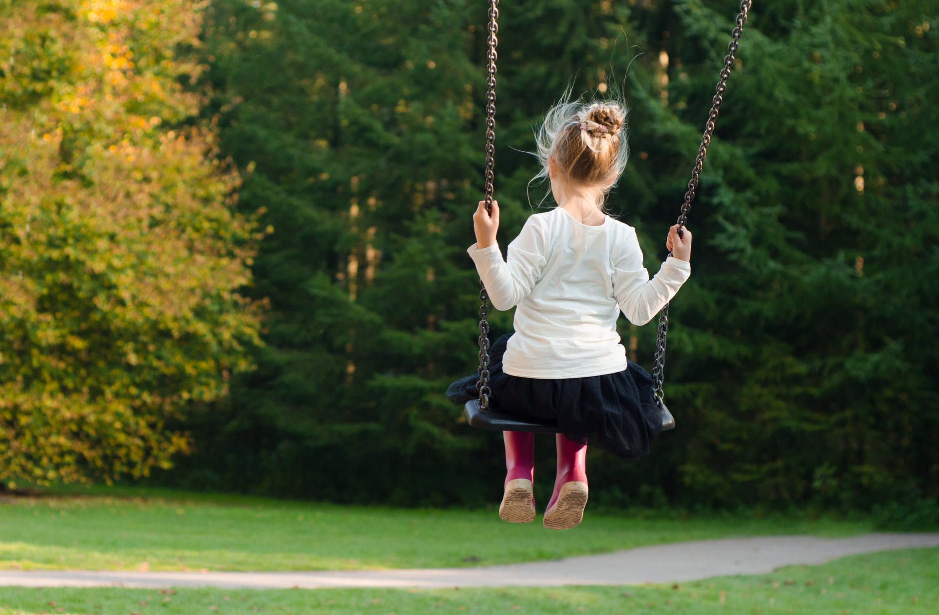 girl in white long sleeve shirt and black skirt sitting on swing during day time